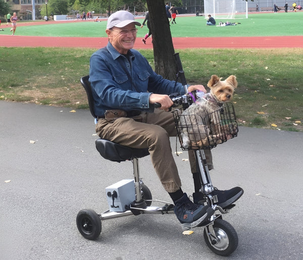 Vista lateral derecha de un hombre mayor conduciendo el scooter de movilidad liviano de viaje SmartScoot por un camino pavimentado en un parque