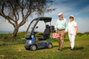 Right Side View Of The AFIKIM Afiscooter C4 Scooter Shown With Optional Hard Top Canopy In The Blue Color With An Elderly Couple Seen Walking On A Grass Field With A Picnic Box On A Sunny Day