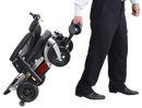 Right Side View Of The FreeRiderUSA Luggie Travel Power Wheelchair Shown In The Folded Position With A Man In Dress Clothes Rolling The Chair