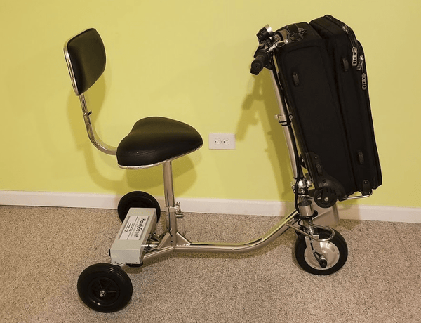 Right Side View Of The HandyScoot Lightweight Travel Mobility Scooter Shown With A Luggage Bag On The Front Luggage Attachment Shown In An Indoor Setting