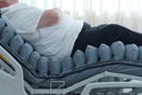 Right Side View Of The Inflated Cells Of The Wellell Domus Auto Pressure Redistribution Mattress System with Quilted Cover Shown With Patient Lying On The Mattress In The Upright Position On An Adjustable Hospital Bed In A Hospital Room