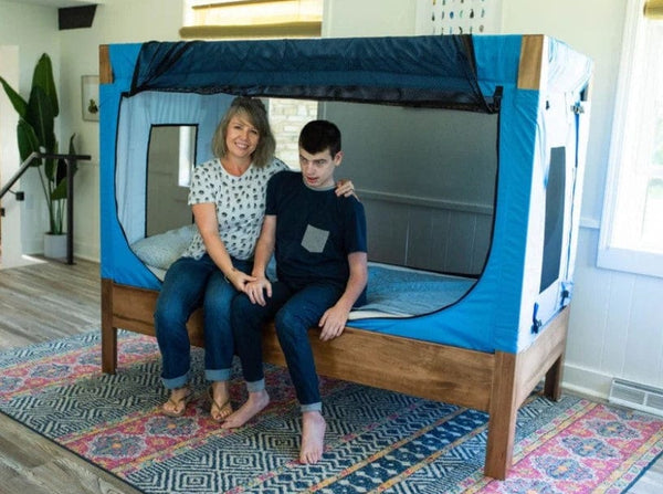 Safe Place Bedding Model 200 Side View Brown Stained Finish Blue Colored Cover With Caregiver And Patient Sitting On Bed