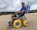 Side View Of The AccessRec TerraWheels All-Terrain Beach Wheelchair Shown With Man Sitting In Chair In A Beach Setting