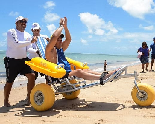 Side View Of The AccessRec WaterWheels Floating Beach Wheelchair Shown With Man Sitting In Chair With Two Men Pushing The Chair On A Sunny Day At The Beach