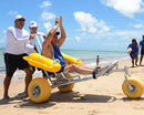 Side View Of The AccessRec WaterWheels Floating Beach Wheelchair Shown With Man Sitting In Chair With Two Men Pushing The Chair On A Sunny Day At The Beach
