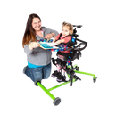 Side View Of The EasyStand Bantam Extra Small Standing Frame Shown In Green Color With Child Using The Device With A Woman Kneeling Next To Her