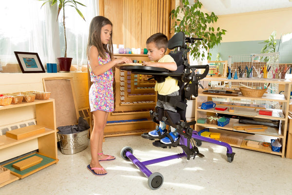 Side View Of The EasyStand Bantam Small Standing Frame Shown In Purple Color With Child In Stander And Young Girl Standing Next To Him