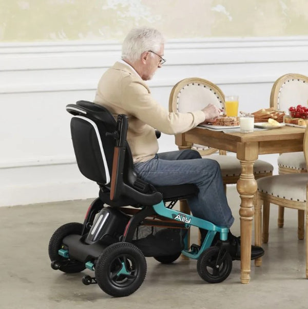 Side View Of The Golden Technologies Ally Electric Wheelchair Shown In Teal Color With Elderly Man Sitting In Chair With An Adjusted Armrest In A Home Setting
