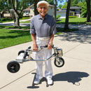 Smiling Senior Holding The HandyScoot Lightweight Travel Mobility Scooter In An Outdoor Setting
