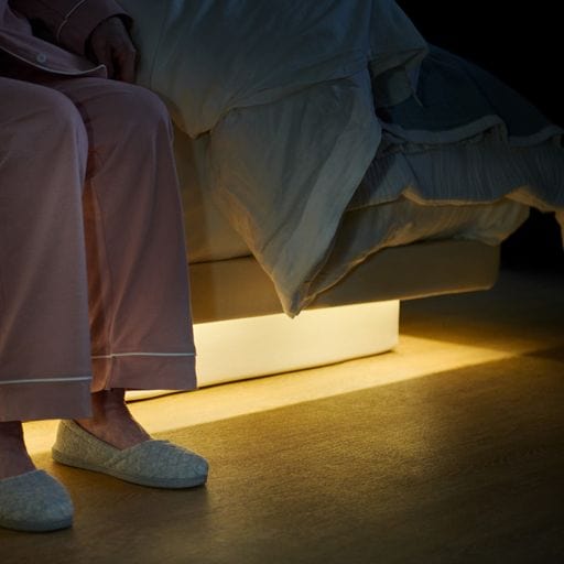 The Dawn House Bed Side View Of Elderly Woman Sitting With Underbed Lighting
