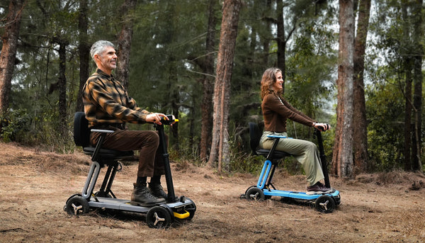 Two People Riding The Paiseec L5 Mobility Scooters One In The Silver And One In The Blue Color In A Forest Setting