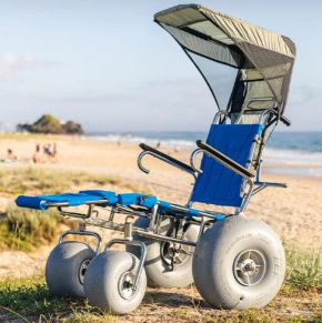 Wheeleez Sandcruiser All-Terrain Beach Wheelchair Side View In Mediterranean Blue Color With Large Balloon Wheels And Canopy, Positioned On A Sandy Beach With Ocean In The Background.  