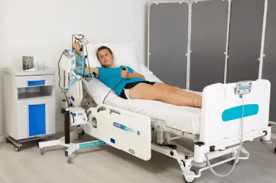 Woman Lying In A Hospital Bed Far View Using The Kinetec 6080 Elbow CPM Machine