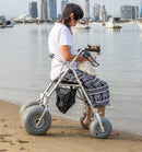 Woman Sitting With Dog On The Wheeleez All-Terrain Beach Rollator Side View With Polyurethane Wheels, Foam Handles, And A Mesh Storage Compartment, Displayed On A Sandy Beach.