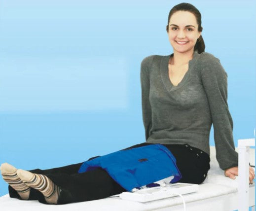 Woman Using The Almagia International ALMAG-2 PEMF Therapy Device On A Medical Table With a Blue Background 