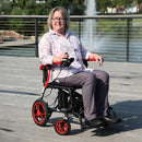 Woman Using The Journey Air Elite Carbon Fiber Electric Wheelchair Shown In Red Trim In A Park Setting