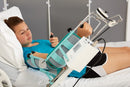 Woman Wearing Shorts And Blue Shirt Lying In A Hospital Bed Using The Kinetec 6080 Elbow CPM Machine