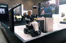 Woman With Robotic Arm Sitting In The STRUTT ev1 Smart Electric Mobility Vehicle Shown In A Convention Center Setting