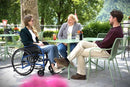 Young Woman Sitting In The Strongback 24 Ultra-Lightweight Wheelchair Shown In A Cafe Setting With Two Other People Sitting In Chairs