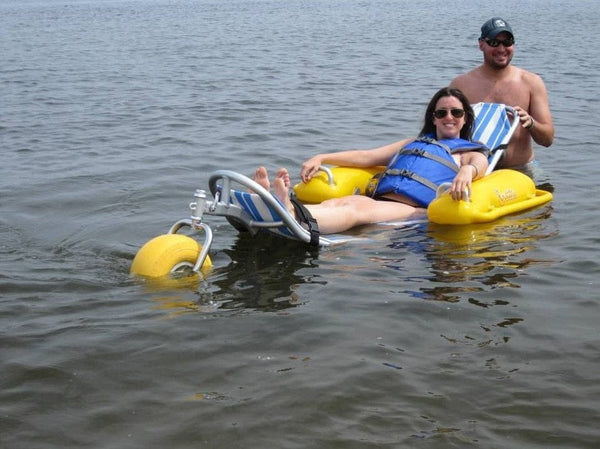 Front View Of The AccessRec WaterWheels Floating Beach Wheelchair Shown With Woman Laying Down In The Chair With Man Standing Behind Her In A Water Setting