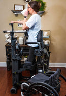 Front View Of The EasyStand Glider Large Active Standing Frame Shown With Woman Using The Device And Drinking Coffee In A Home Setting
