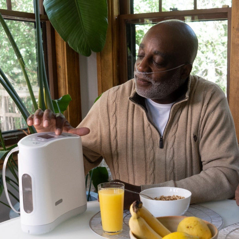 Front View Of The O2 Concepts Oxilife Liberty Portable Oxygen Concentrator Shown With A Man Operating The Machine In A Home Setting