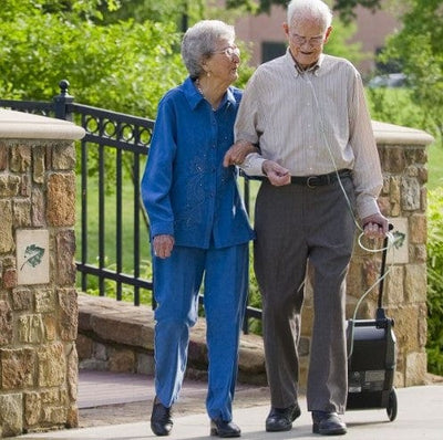 Front View Of The O2 Concepts Oxlife Independence Oxygen Concentrator In An Outdoor Setting Shown With A Man And A Woman Walking Together