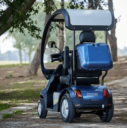 Rear Left Side View Of The AFIKIM Afiscooter S4 Scooter Shown In The Blue Color With Optional Rear Lock Box And Hard Top Canopy In An Outdoor Setting