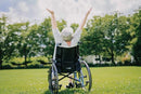 Rear View Of Elderly Woman Raising Her Hands In A Joyous Moment While Sitting In An Outdoor Setting On The Strongback 24 Flip Back Arms Ultra-Lightweight Wheelchair