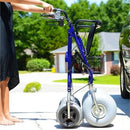Right Side View Of The Debug Mobility All-Terrain Beach Rollator In The Folded Position With A Woman Holding The Handles In A Neighborhood Setting