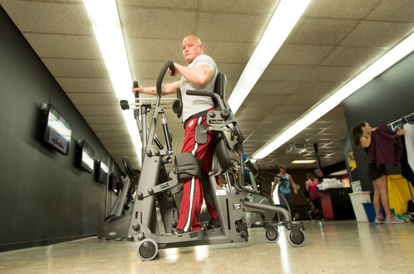 Side View Of The EasyStand Glider Large Active Standing Frame Shown With Man Using Device In A Gym Setting