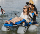 Wheeleez Sandcruiser All-Terrain Beach Wheelchair Front View In Mediterranean Blue Color With Large Balloon Wheels, Positioned In The Water With One Woman Sitting In The Sandcruiser And Woman Pushing The Wheelchair On A Sunny Day.