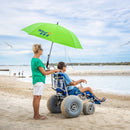 Wheeleez Sandcruiser All-Terrain Beach Wheelchair Rear View In Mediterranean Blue Color With Large Balloon Wheels, RoboCup Holder, and Umbrella, Positioned On A Sandy Beach With Man Sitting In The Wheelchair While A Woman Stands Behind The Wheelchair Holding The Handles With Ocean