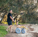 Wheeleez Sandpiper All-Terrain Beach Wheelchair Side View Yellow And Silver Color With Large Wheels Designed For Children And Small Adults On A Sandy Beach Man Pushing Wheelchair With Young Girl Sitting.