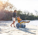 Wheeleez Sandpiper All-Terrain Beach Wheelchair Side View Yellow And Silver Color With Large Wheels Designed For Children And Small Adults On A Sandy Beach Woman Pushing Wheelchair With Young Boy Sitting.