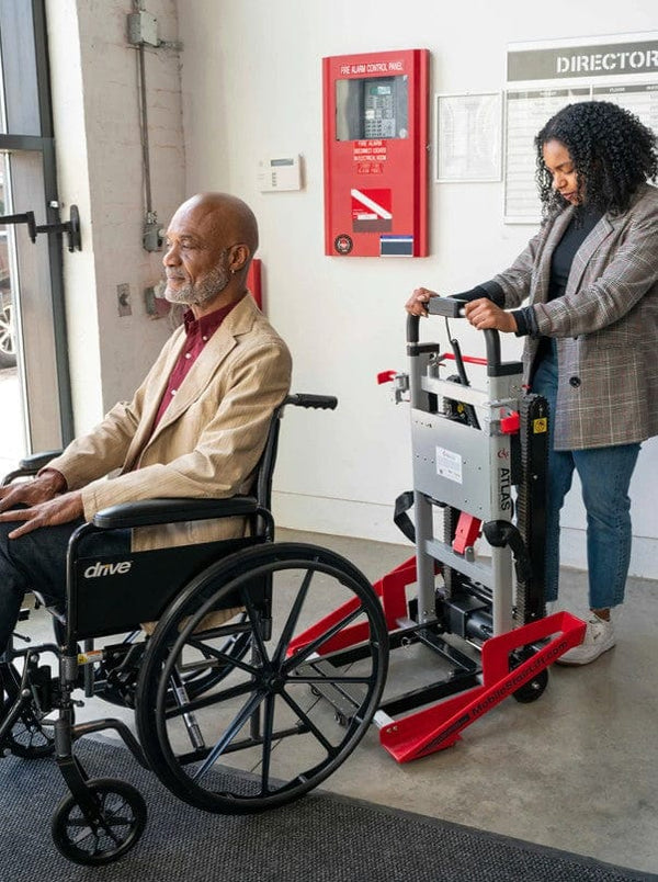 Woman Using The Atlas Stair Climbing Wheelchair Lift To Assist An Elderly Man In A Wheelchair